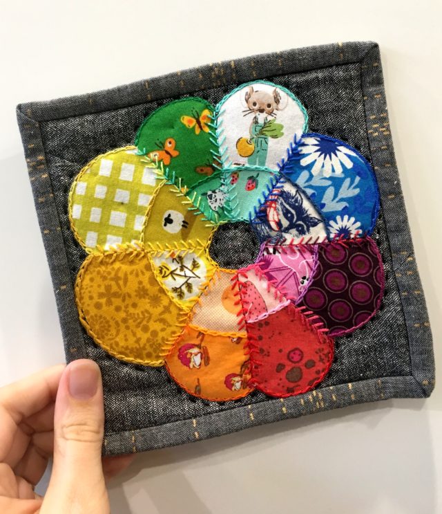 Handmade mug rug featuring rainbow curved dresdens, fussy cutting, and embroidery by cailtinpolden