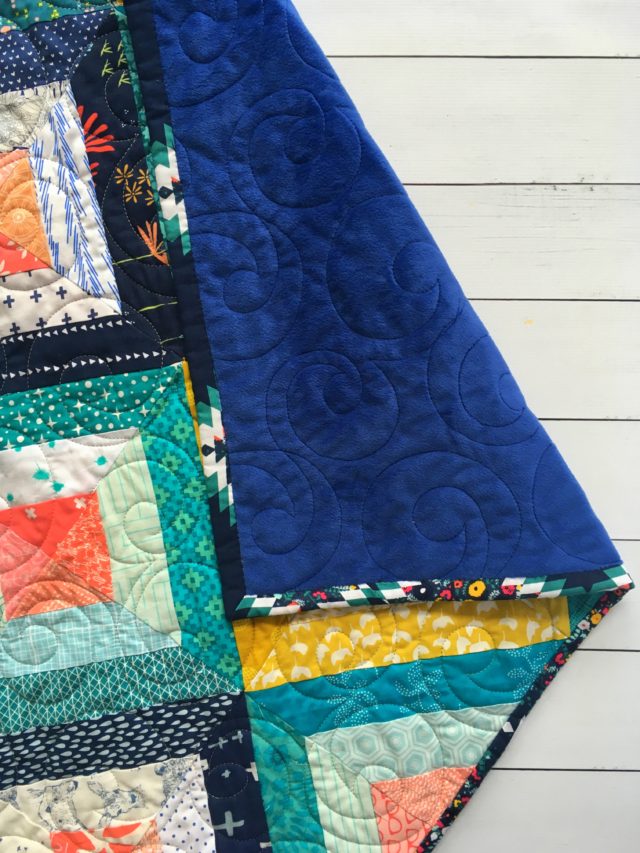 Scrap quilt in navy, teal, mustard, coral with navy minky backing using the Treasure Hunt quilt block pattern on BlossomHeartQuilts.com