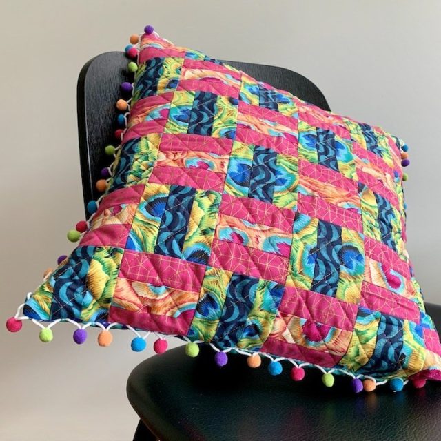Strip pieced quilted pillow with pompom trim